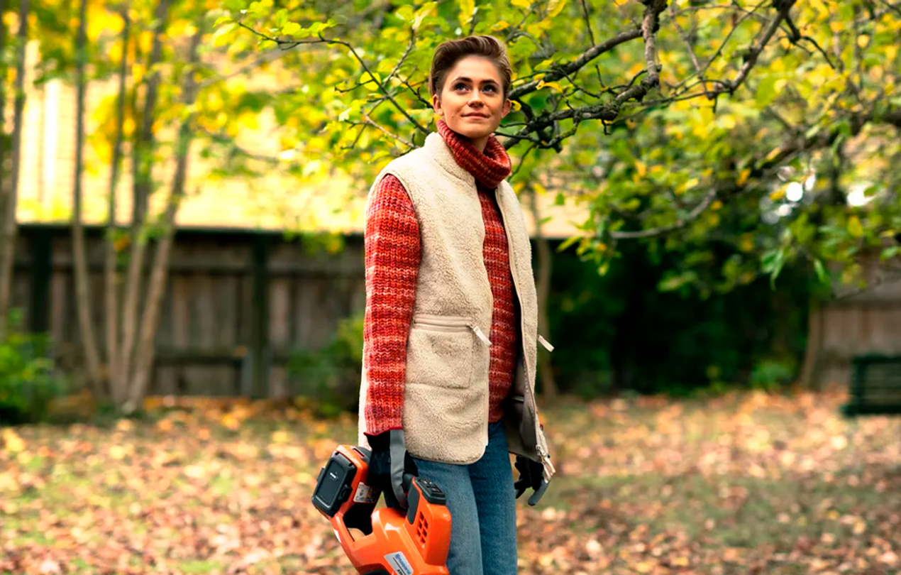 Nainen lehtipuhallin kädessä syksyisessä maisemassa.