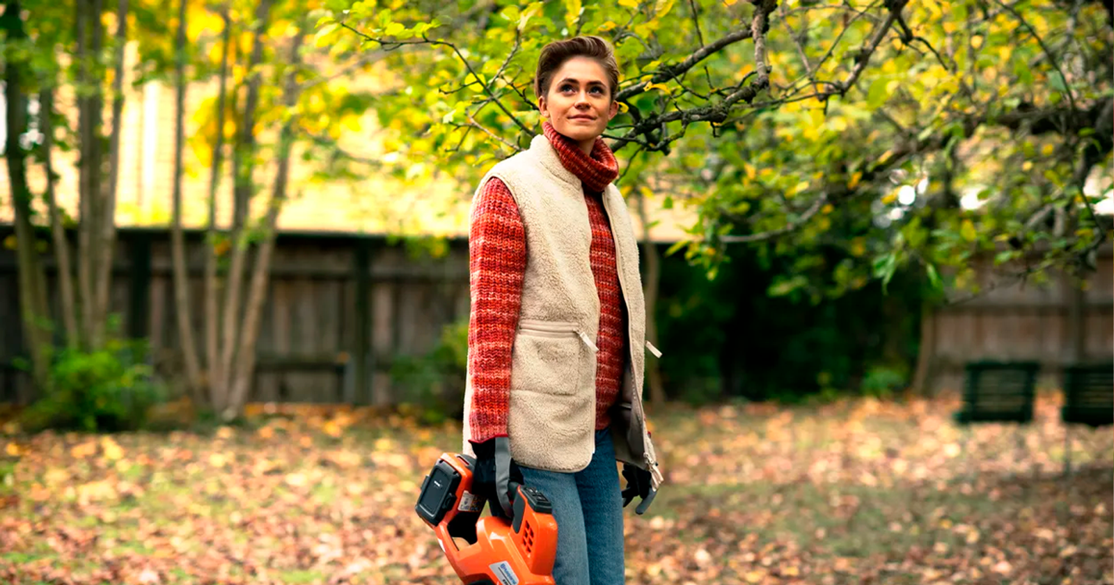 Nainen lehtipuhallin kädessä pihalla.